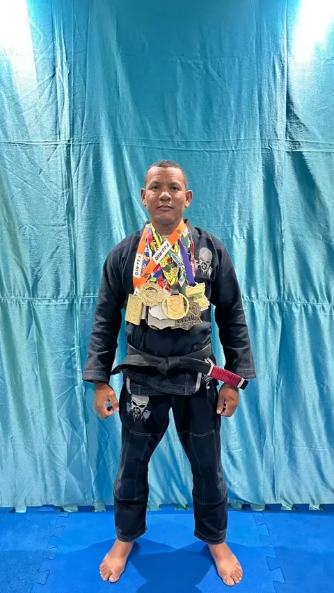 Professor Gilson Batista, faixa preta, com medalhas e cinturões de jiu-jitsu