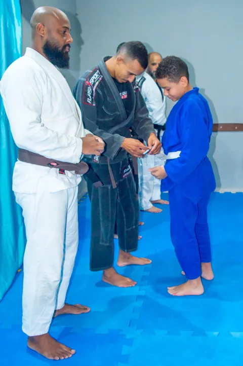 Criança recebendo a faixa das mãos dos professores em graduação de jiu-jitsu infantil